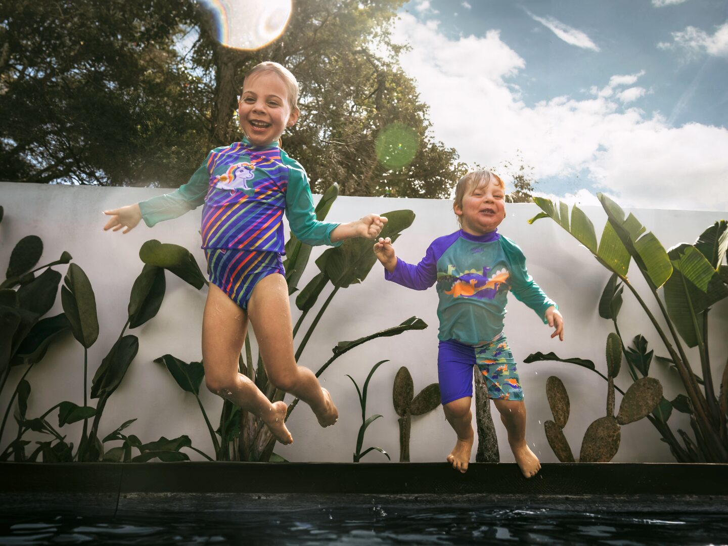 two children jumping into a pool wearing Speedo swimwear