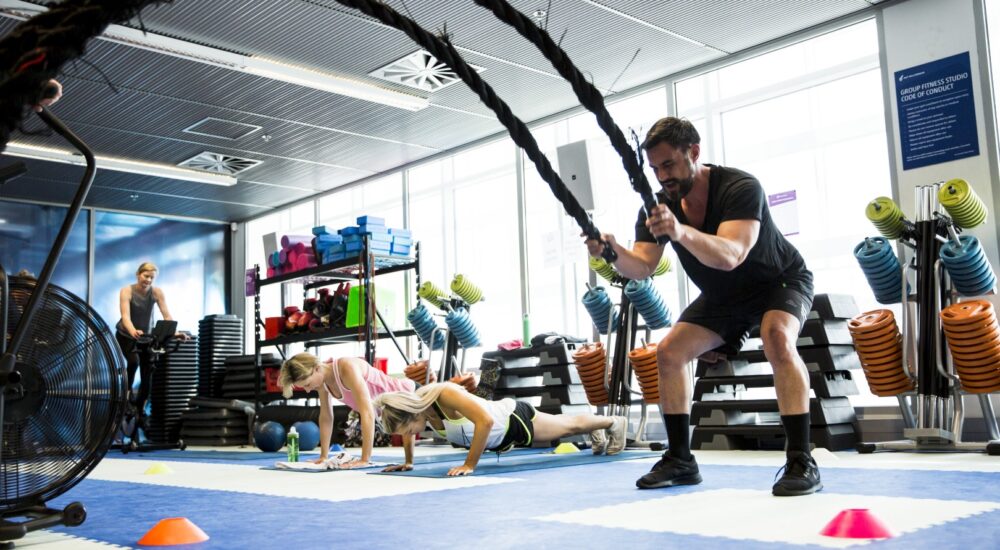 Gym member on the battle rope exercise in a circuit class. Other gym members in the background completing their circuits.