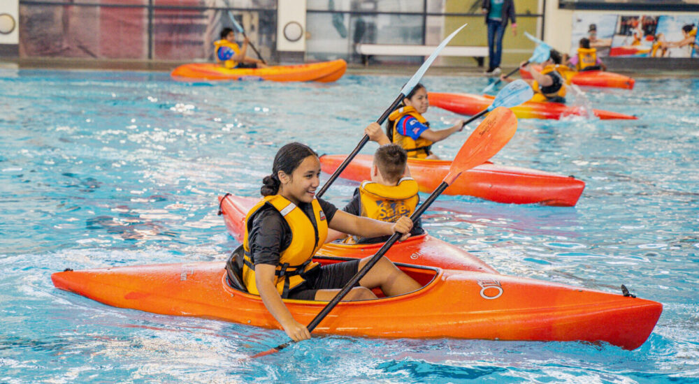 Children paddle around the pool in a kayak