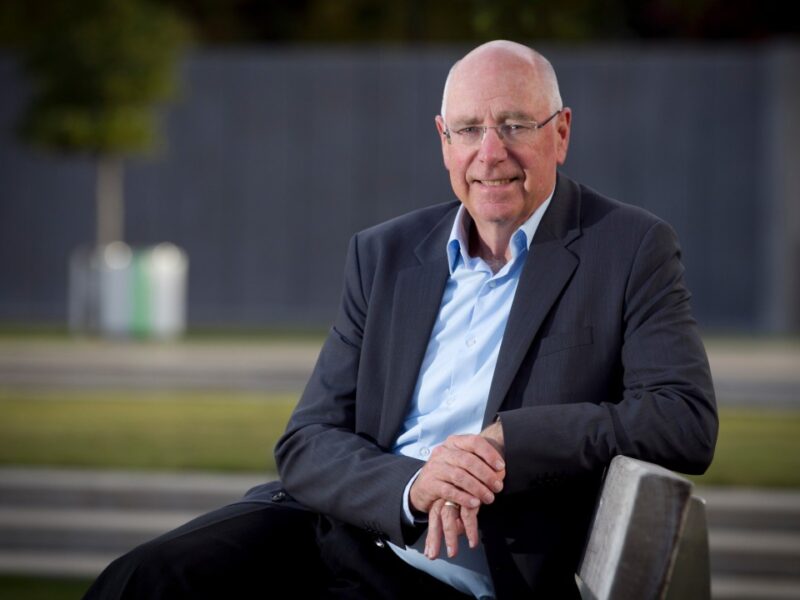 Sir Stephen Tindall seated on a bench, smiling at the camera