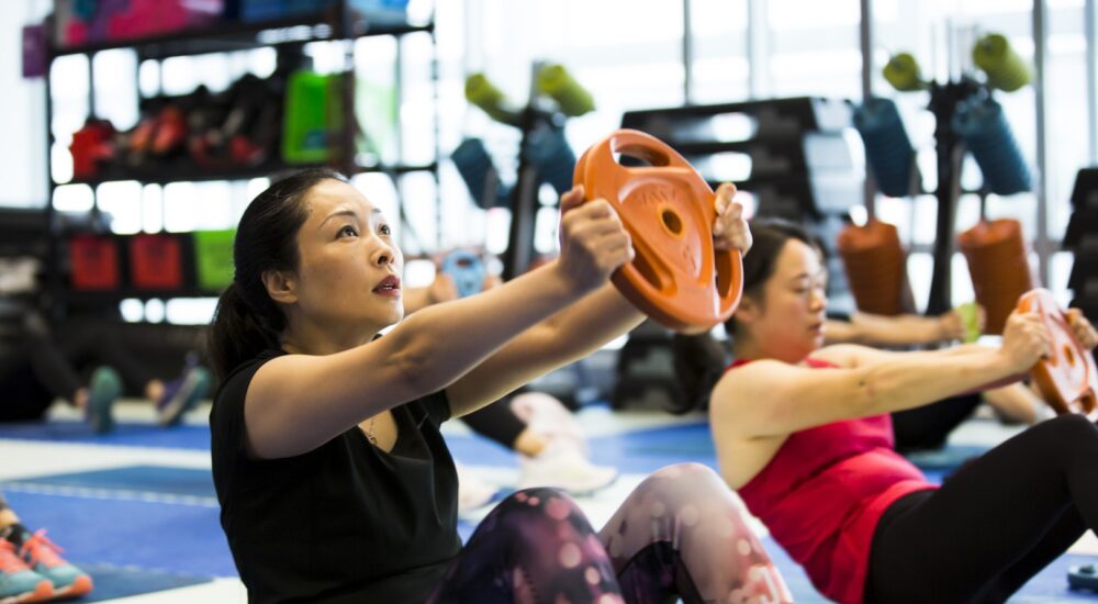 Two gym members in a core class holding a weight out in front of them