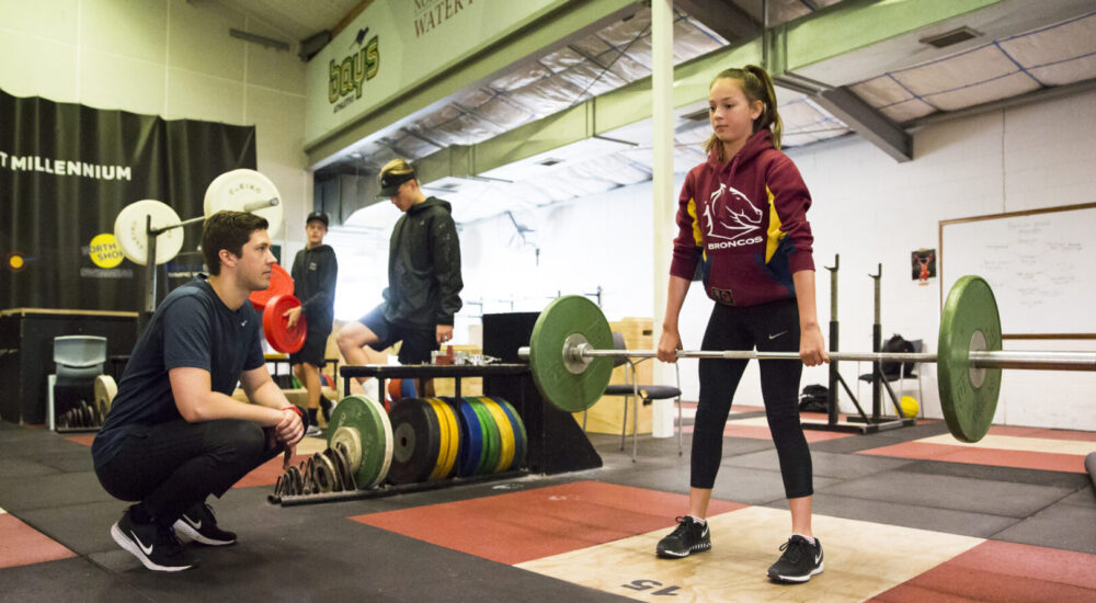 Athlete Development coach observes an athlete lifting a barbell