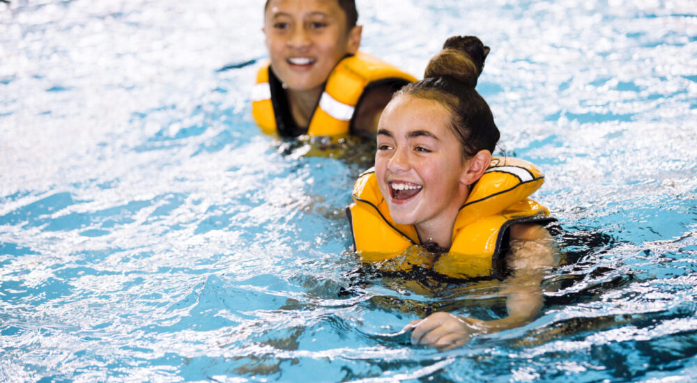 Two children in the pool wearing life jackets and smiling