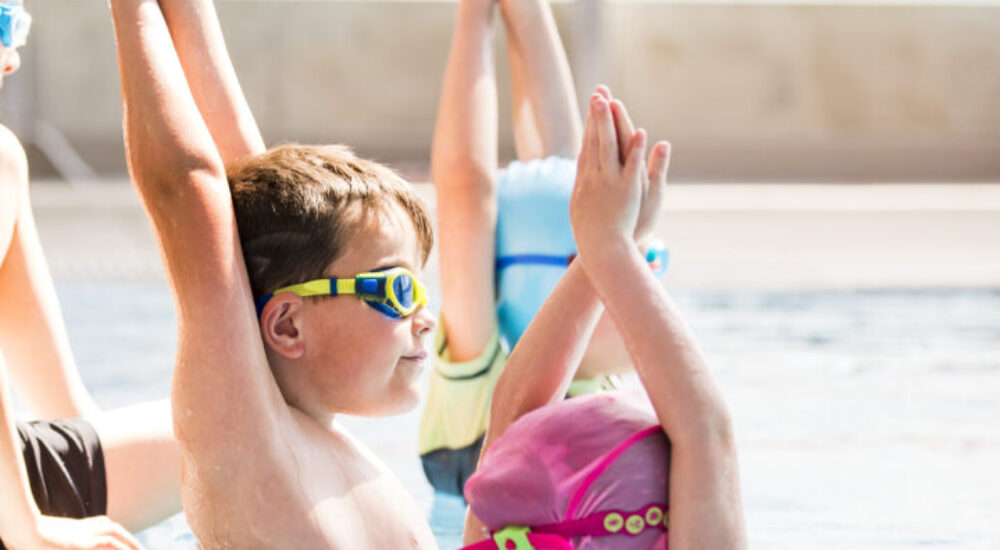 Three children in a swimming lessons with their arms above their head in a streamline position