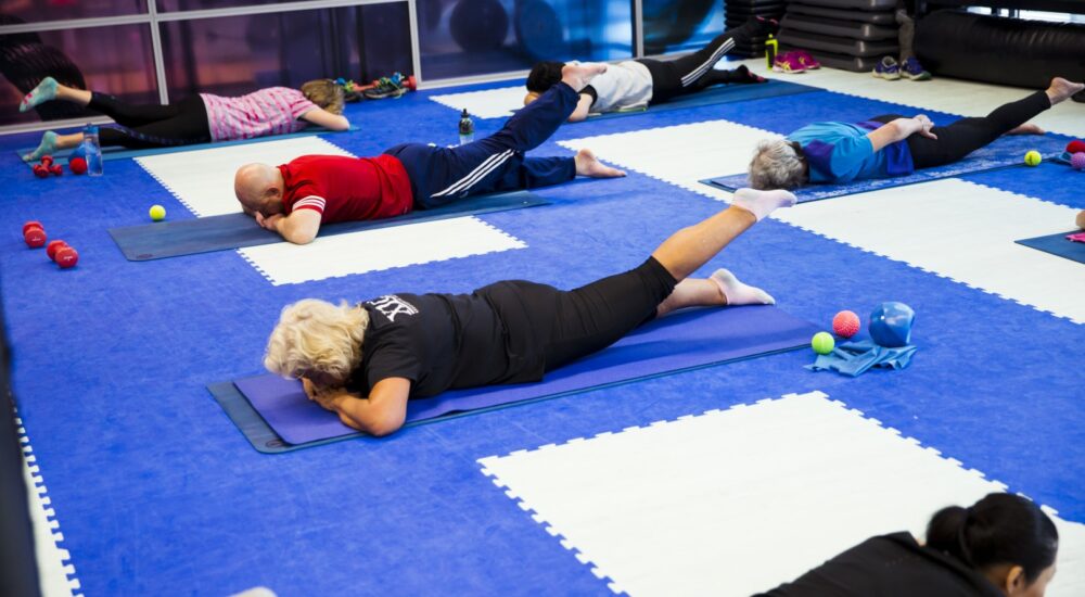 Gym members lying down with one leg up off the group as they participate in a pilates class