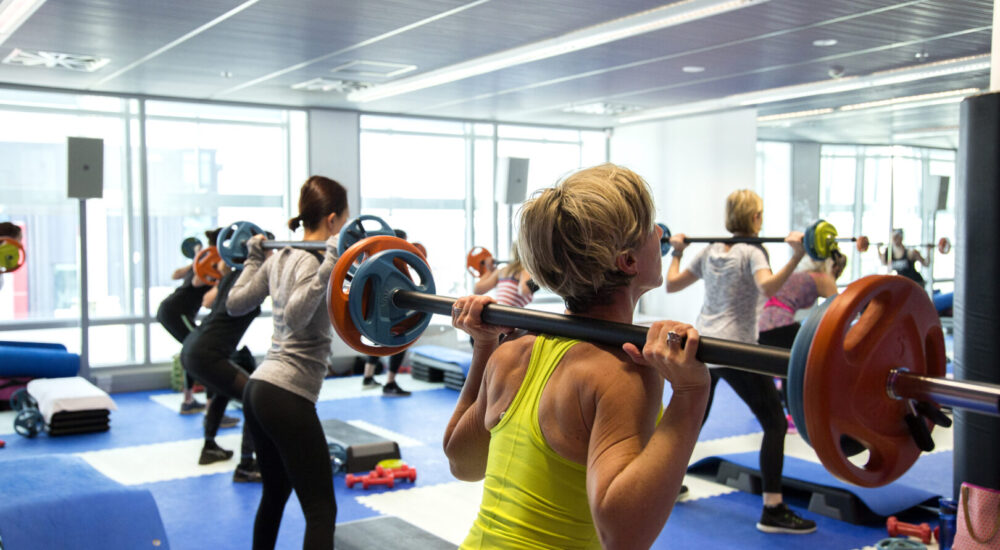 Pump class, participants have a weighted barbell on their shoulders