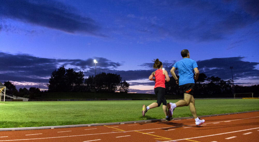 Two running group participants running around the track side by side