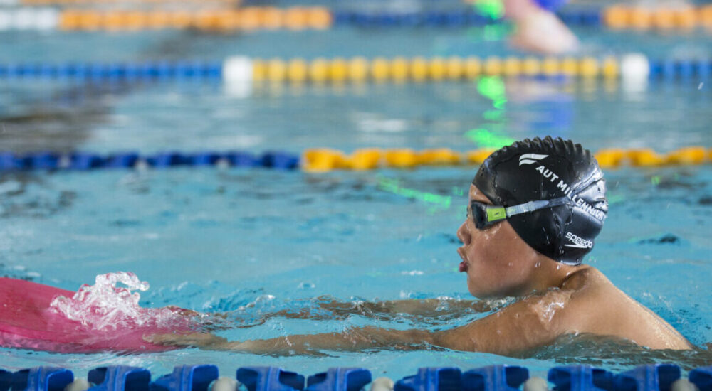 A child in the pool practices kicking while holding onto a kickboard